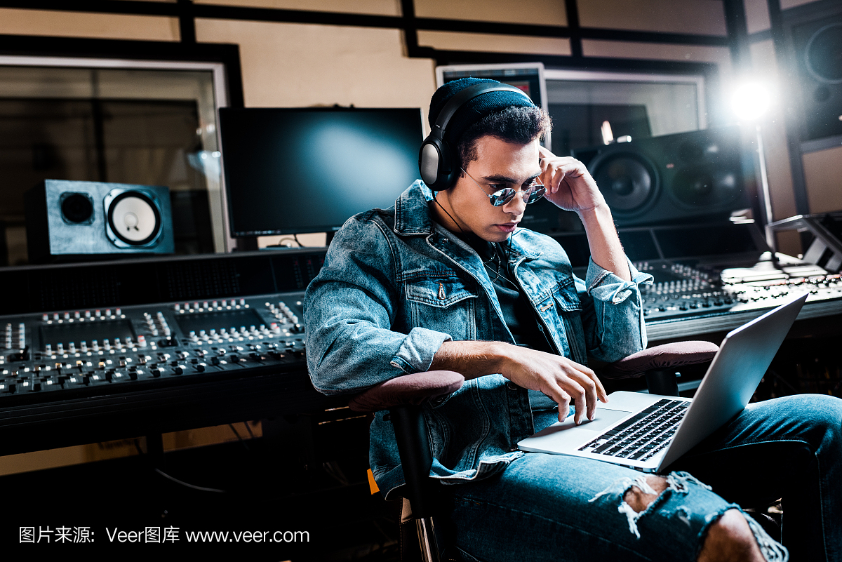 集中混合种族声音制作人耳机使用笔记本电脑在录音室